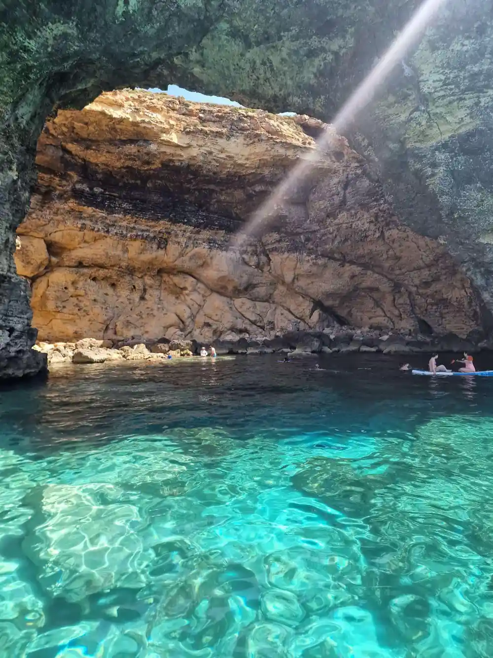 A cliff and swimmers in bright shallow water